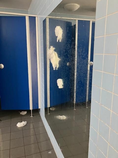 Nasse Papierklumpen kleben an einer blauen Kabinentür, Papier auf dem Boden.
