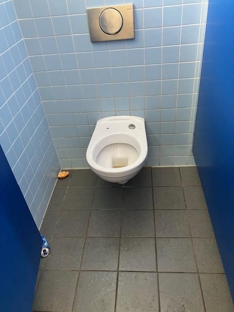 Toilettenkabine mit hellblauen Fliesen, Toilette ohne Brille, Reste auf dem Boden.