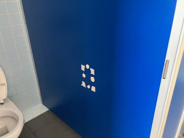 Blaue Wand mit Bohrlöchern, an denen ein Spender hing.