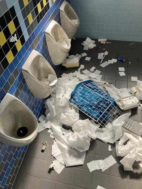 Urinale mit Papier auf dem Boden, derselbe Raum wie auf Bild 5, aus anderem Winkel.