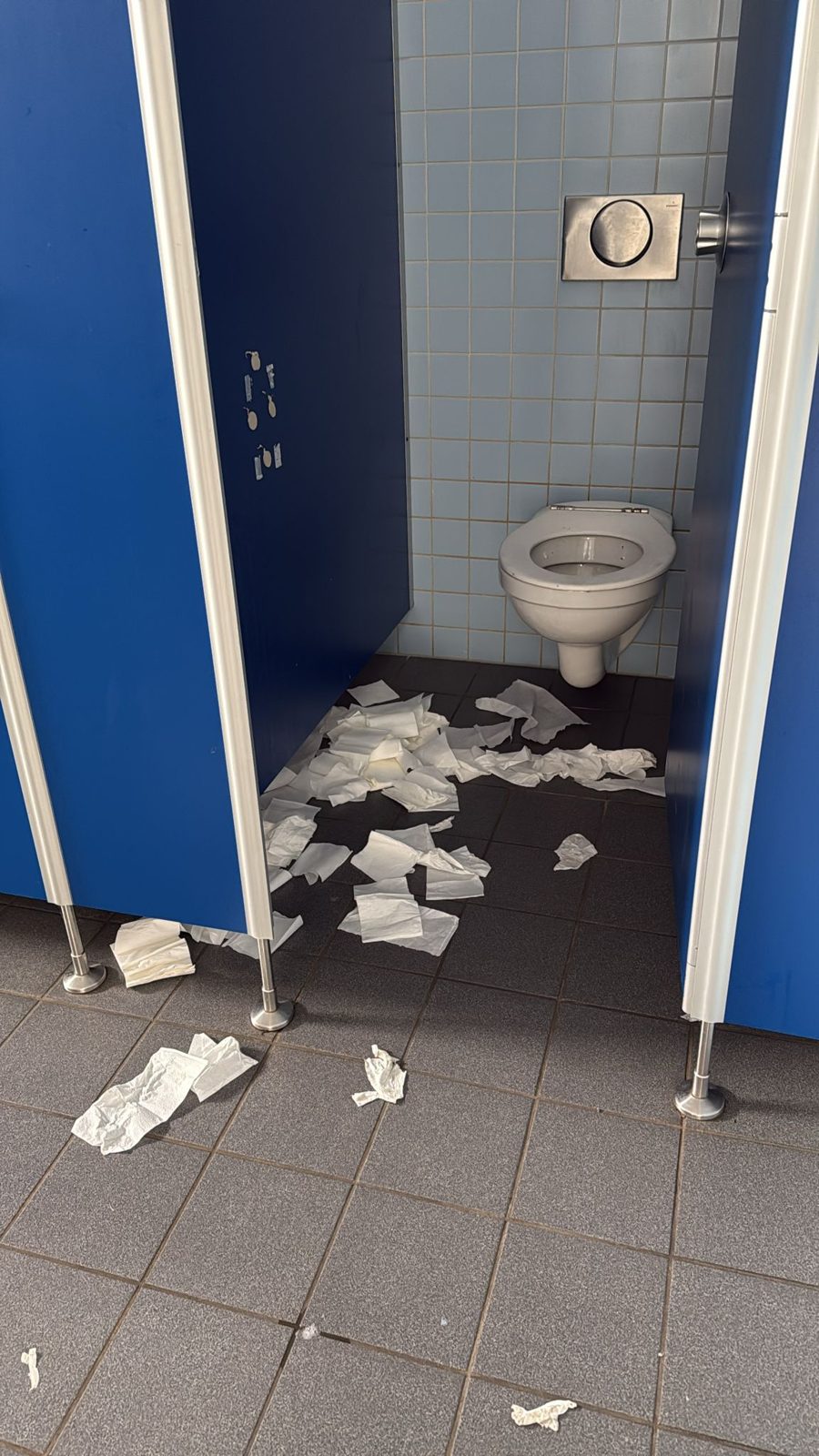 Kabine mit Papier auf dem Boden, Toilette im Hintergrund.