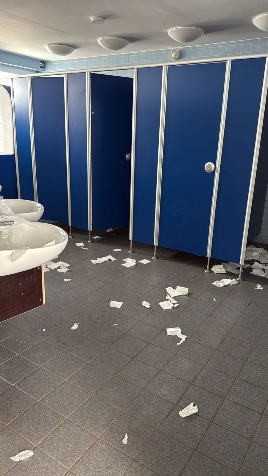 Reihe blauer Kabinen, Papier auf dem Boden, Waschbecken links.